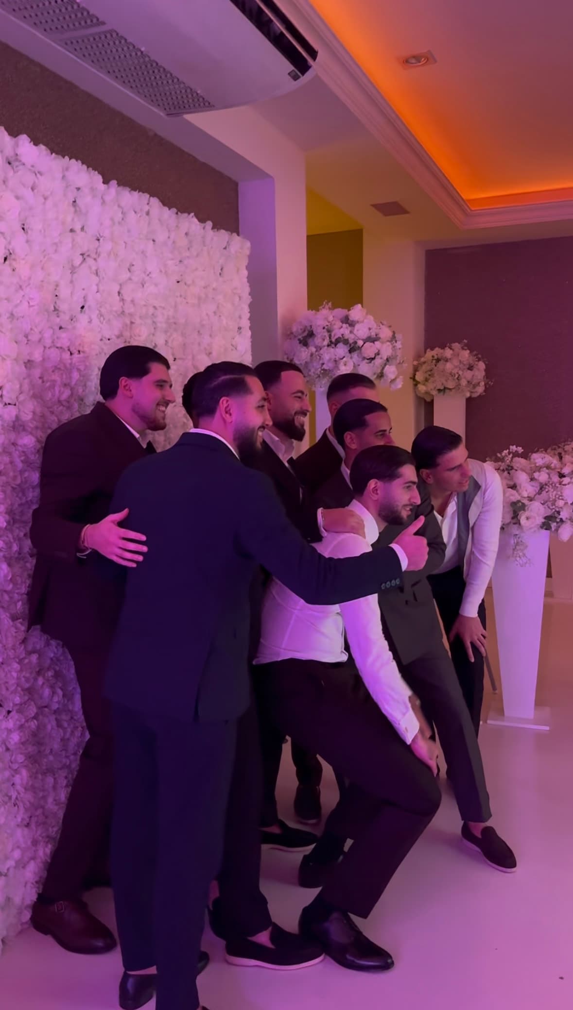 Bruiloftsgasten poseren samen voor een witte flowerwall